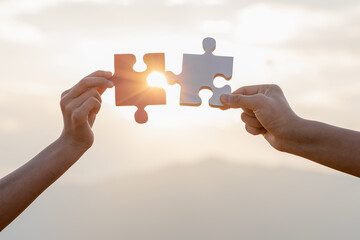 Hands holding piece of blank jigsaw puzzle at sunset background
