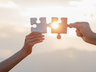 Hands holding piece of blank jigsaw puzzle at sunset background
