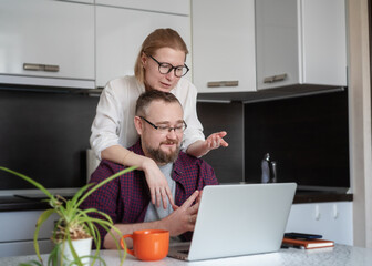 Young adult couple husband and wife tsitting in the kitchen and looking at a laptop screen., checking banking online application on a laptop