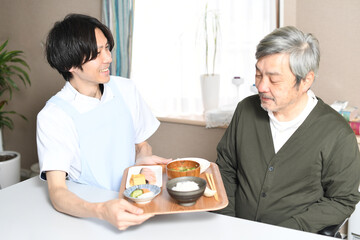 食事を運ぶ男性介護士と高齢者の白髪男性