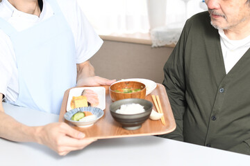 食事を運ぶ男性介護士と高齢者の白髪男性