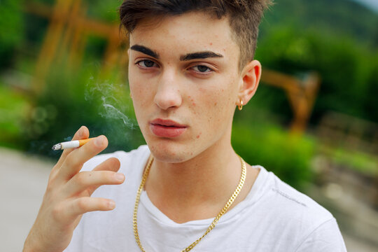 Serious young man smoking a cigarette outdoors exhaling the smok