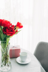 Bouquet of red tulips on table and white coffee cup. Concept for greeting card