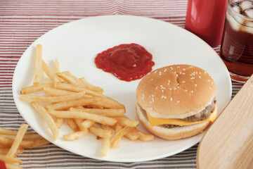 Close-up shot: Ketchup poured into  white empty dish placed on a tablecloth. To eat with junk food placed next to it, such as French fries, hamburgers, and cola, which are unhealthy fast foods.