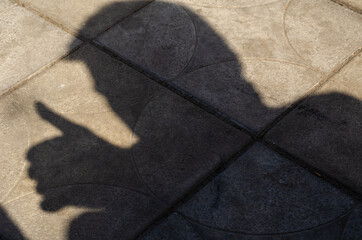 Male shadow on the sidewalk with a thumb up gesture.