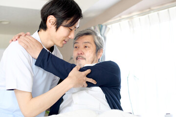 ベッドでお年寄りの男性を起こす介護士の男性