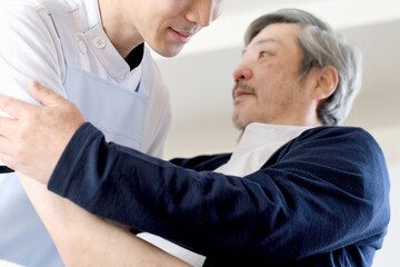 Obraz premium ベッドでお年寄りの男性を起こす介護士の男性