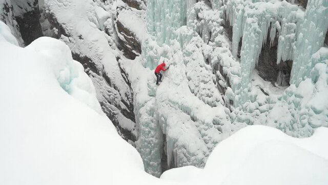 Ice climber climbing on frozen waterfall in snowy winter landscape of Ouray Ice Park, Colorado USA, wide view