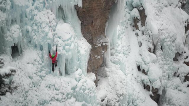 Ice climber with axe climbing on frozen waterfall in cold snowy winter landscape wide view