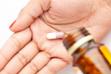 Macro Close up of medicinal or herbal  color tablet, capsule and pill are coming out from amber glass bottle on a female hand palm. Top view,