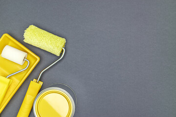 can of yellow paint with yellow paint rollers and tray on gray background. renovation concept.