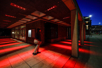 Halmstad, Sweden, A man on a street corner lit up at night in the color red.