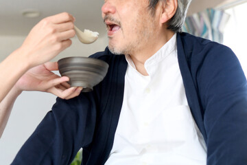 シニア男性に食事の介助をするエプロン姿の若い男性