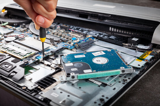 A computer technician is repairing an old laptop using a screw driver. Closeup isolated image showing complex interior of a laptop with circuit boards and delicate items. The person removes a screw.