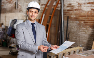 Portrait of friendly man in suit and helmet holding paper at construction site