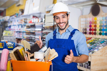 Happy smiling workman holding basket with picked tools in paint store