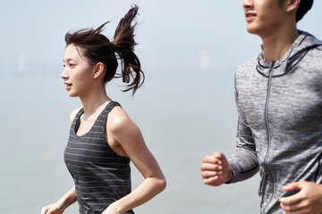 young asian man and woman running outdoors by the sea