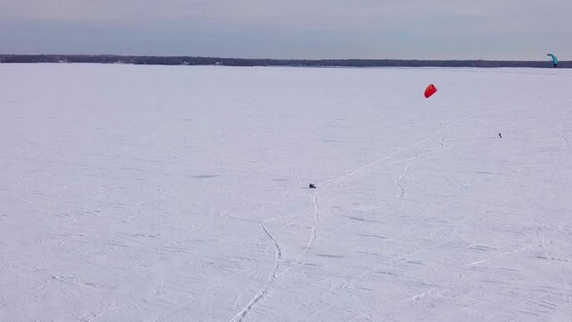 Two kite sufer on the frozen lake in winter making tracks in the white snow