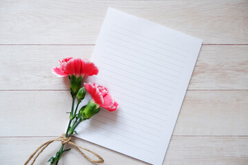 Empty letter papers with carnation flowers and on wooden background. Mother’s Day, Father’s Day. ウッドテーブルを背景にカードとピンクカーネーション、母の日、グリーティング