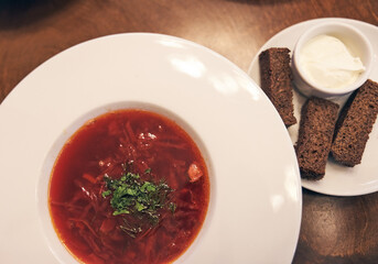 A traditional dish of Russian and Ukrainian cuisine. Borscht with herbs, sour cream and garlic croutons. On a wooden table with copy space