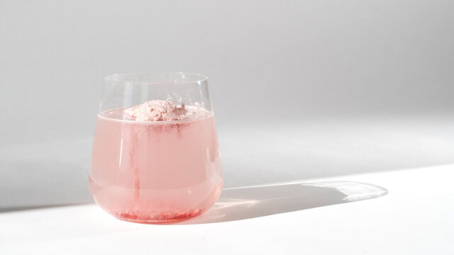 Super food. Glass of natural strawberry collagen protein powder in glass of water for skin regeneration. Trendy food additives. White background with sunlight and deep shadow of glass. Hard sunlight.
