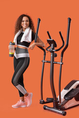 Beautiful young woman with bottle of water and elliptical machine on color background