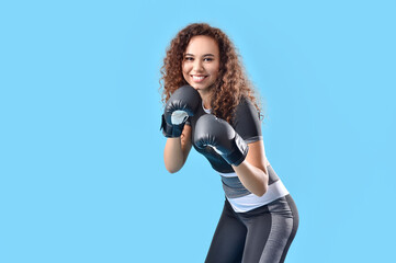 Beautiful young woman in boxing gloves on color background