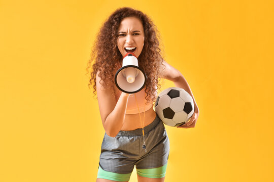 Beautiful young woman with megaphone and soccer ball on color background