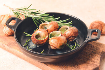 Frying pan with tasty snails on color background, closeup