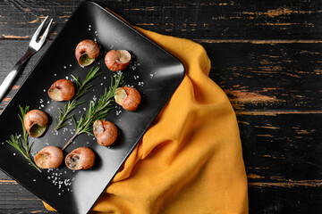 Plate with tasty snails on dark wooden background