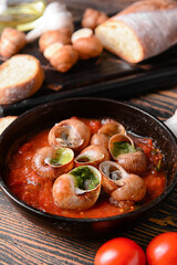 Frying pan with tasty snails on wooden background, closeup
