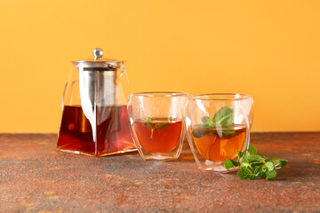 Teapot and cups of hot beverage on color background