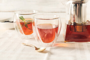 Teapot and cups of hot beverage on light background