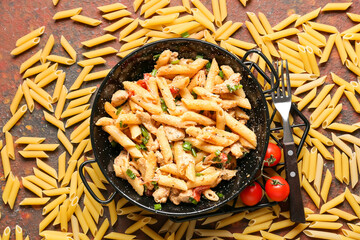 Frying pan with tasty cajun chicken pasta on grunge background