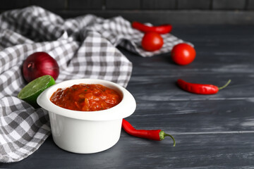 Bowl of tasty salsa sauce on dark wooden background