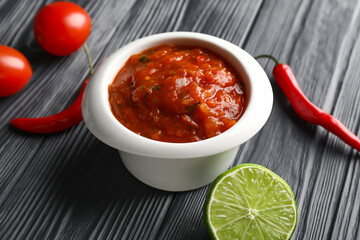 Bowl of tasty salsa sauce on dark wooden background