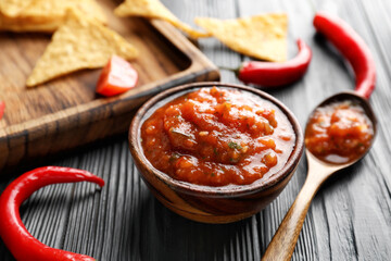 Bowl of tasty salsa sauce with nachos on dark wooden background