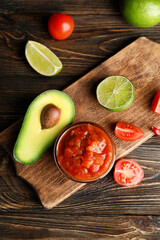 Bowl of tasty salsa sauce with ingredients on wooden background