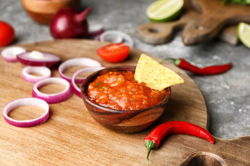 Bowl of tasty salsa sauce with ingredients and nachos on grunge background