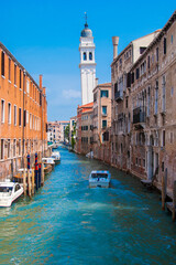 Fototapeta na wymiar One of many canals and aged houses in Venice at sunny day, San Giorgio dei Greci tower on background