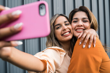 Two friends taking selfie with phone outdoors.