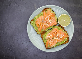 The concept is useful, tasty breakfast. Toasted bread with avocado, red fish. Bruschetta with avocado, trout on a marble surface. Whole grain bread with avocado paste, lime and salmon. Top view