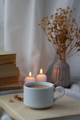 A cup of coffee, books, a bouquet of flowers and candles on the table. Composition in brown-beige tones. Stylish still life, blog life concept.