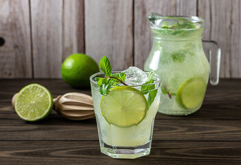 Homemade lemonade with lime, mint in a glass with a jug on a wooden rustic table. Summer refreshing drink. - obrazy, fototapety, plakaty