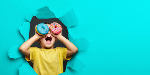 Happy cute boy is having fun played with donuts on black background wall. Bright photo of a child.