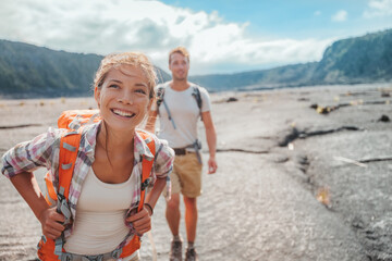 Hiking couple walking with backpacks on lava field trail in Hawaii. Summer travel happy smiling Asian girl and man hikers outdoor adventure on Big Island, USA. - 427160524