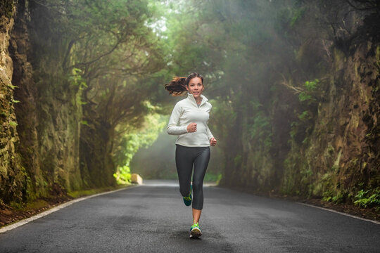 Running woman in autumn forest training on cold morning. Outdoor sport Asian girl athlete runner jogging outside fitness winter motivation.