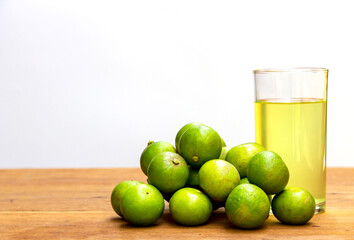 pile of green lemons on a rustic wooden table with a glass of lemon juice. Lemon has medicinal properties and vitamin C