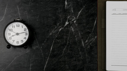 A clock and planner book on black marble surface. Concept for time management. 