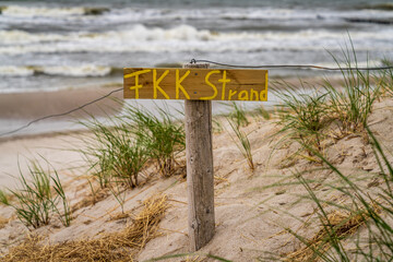 Sign: FKK Strand (German for 'naturist beach'), with dunes and sand in the background